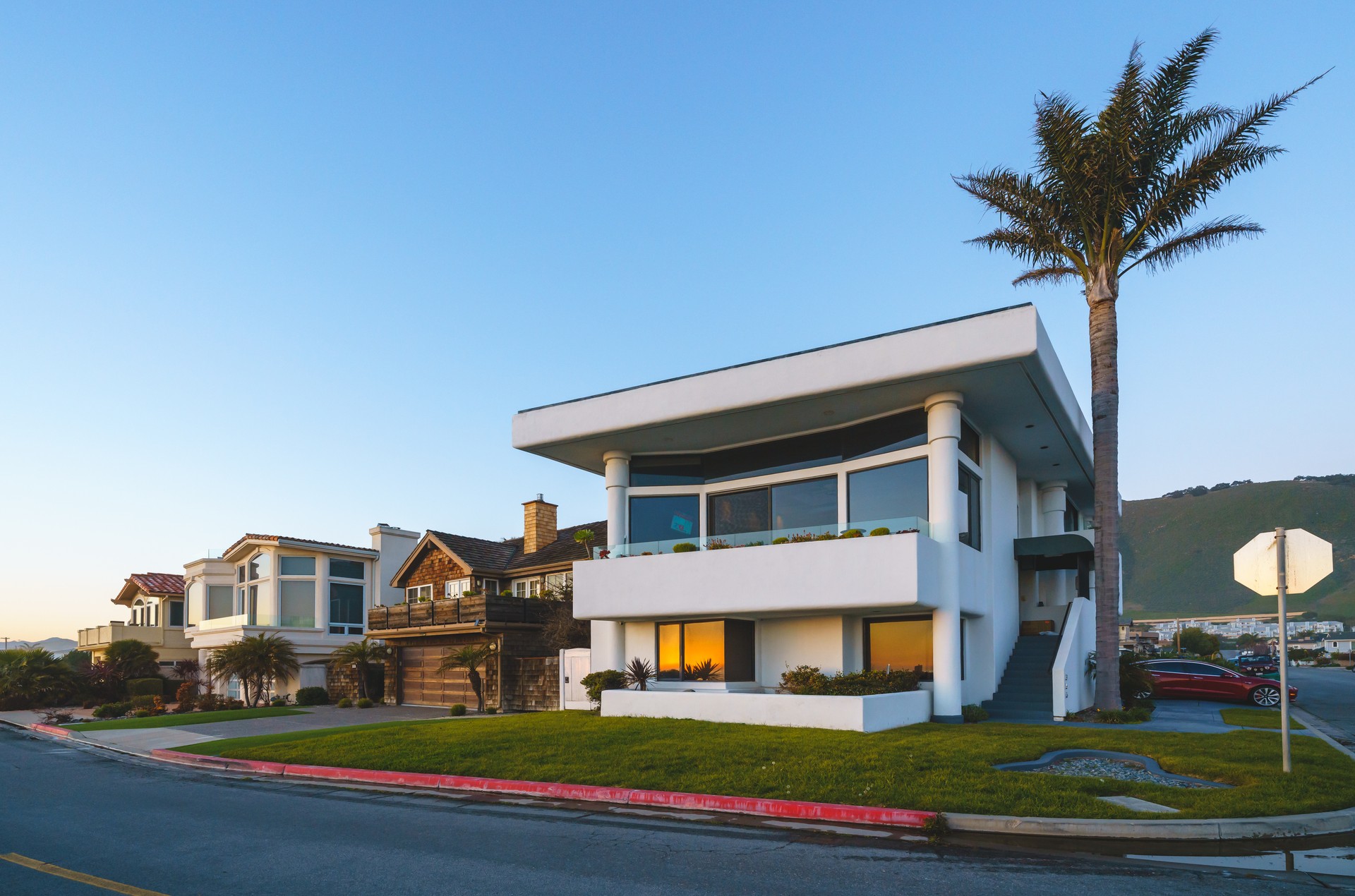 Beautiful houses with ocean views, with nicely landscaped front the yard, palm trees and clear sky in the background, in a small beach town somewhere in California at sunset