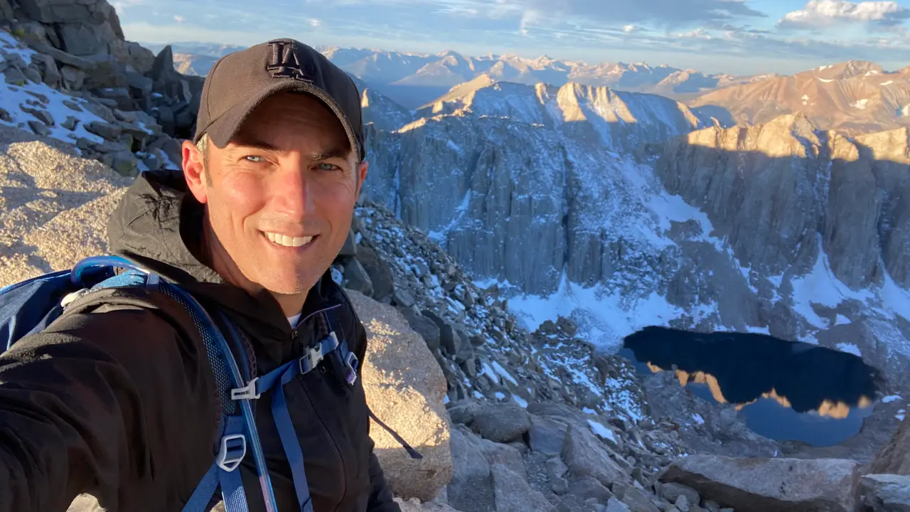 Corbett hiking near the summit of Mount Whitney with alpine lake and rugged Sierra Nevada peaks in the background